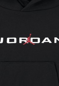 Must seljakott, mille ees on tasku, millel on valged "JORDAN" tähed. Punane Jumpmani logo asub "JORDAN" sõna kohal, tähe "A" kohal.