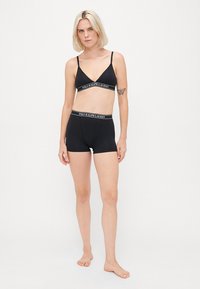 Svart bomulls-bh og matchende shorts med elastisk midje. Har en kontrasterende logo-belte øverst, minimalistisk design.