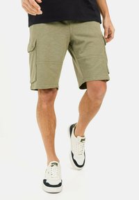Oliven grønne cargo shorts med to sidelommer, lige pasform og et let tekstureret stof. Bæres med hvide sneakers med marineblå accenter.
