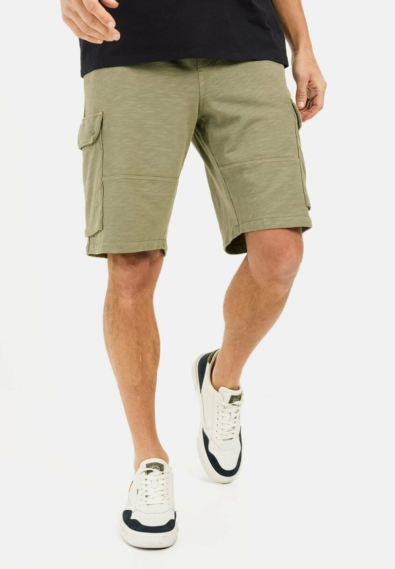 Olivgrüne Cargo-Shorts mit zwei seitlichen Taschen, gerader Schnitt und leicht strukturiertem Stoff. Getragen mit weißen Sneakern mit Navy-Akzenten.