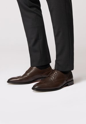 Braune Lederdressschuhe mit Broguemuster, flachen Schnürsenkeln und runder Zehenpartie, kombiniert mit dunklen maßgeschneiderten Hosen.