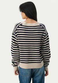 Pull rayé crème et marine, avec un col rond ribbé et des poignets, coupe décontractée et texture en tricot douce. Un jean bleu est porté en dessous.