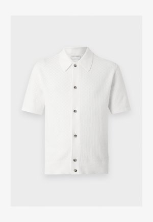 Chemise en maille blanche à manches courtes avec col et six boutons sur le devant, présentant un motif texturé subtil sur le tissu.