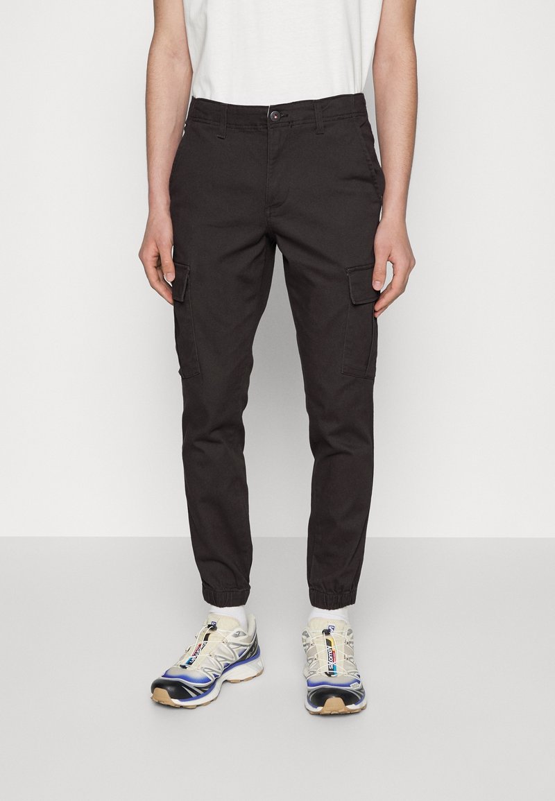 Czarne spodnie typu cargo wykonane z bawełny, z bocznymi kieszeniami i elastycznymi mankietami, w zestawieniu z wielokolorowymi sneakersami z teksturowaną podeszwą.