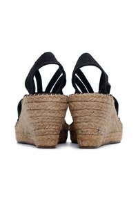Sandały na koturnie z czarną tkaniną u góry, otwartym tyłem i plecioną podeszwą z juty. Teksturowany obcas o zaokrąglonym kształcie oraz elastyczne paski wokół kostki.