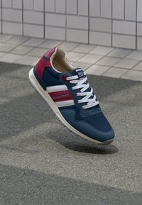 Navy and burgundy athletic sneaker with a mesh upper, white accents, and a textured sole. Features laces and branding on the tongue.