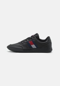 Sneakers neri in pelle con una texture liscia. Presentano un motivo a strisce diagonali colorate in rosso, bianco e blu sul lato.