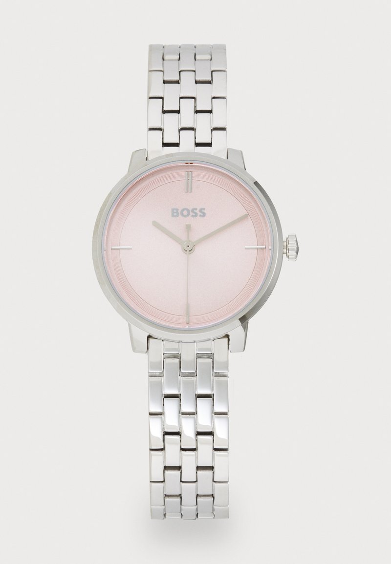 Montre bracelet en argent avec un cadran rose, dotée d'un design minimaliste, de marqueurs d'heure en argent et d'un bracelet à maillons en métal. Logo de la marque affiché.