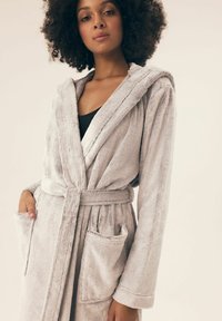 Jasnoszary, pluszowy szlafrok z kapturem, przednimi kieszeniami i paskiem do związania. Miękka faktura z haftowanym wykończeniem na brzegach.