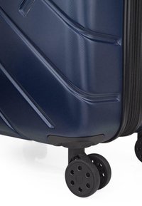 Maletín rígido de color azul marino con superficie texturizada, líneas curvadas, dos ruedas negras y un cierre con cremallera en un lado.