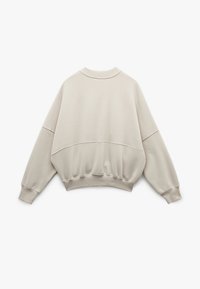 Lys beige oversized sweatshirt med rund hals, sænkede skuldre, ribbede manchetter og en samlet kant. Glat bomuldsstof.