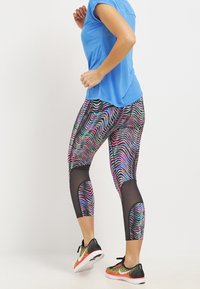 Colorful, patterned leggings in black, pink, and blue, featuring mesh panels. Paired with a blue top and black athletic shoes.
