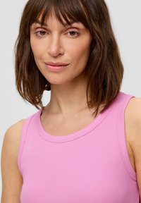 Aansluitend roze tanktop met een geribbelde textuur, ronde hals en brede schouderbanden. De stof ziet er glad en rekbaar uit, geschikt voor casual kleding.