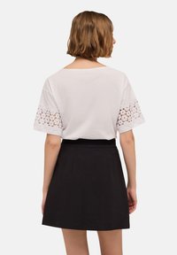 Top blanco de manga corta con detalles de encaje en las mangas, combinado con una falda negra de talle alto. Tejido suave, corte relajado.