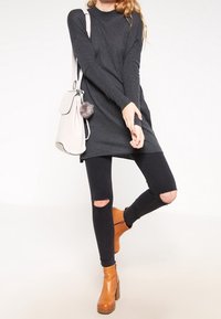 Tunic di colore grigio carbone a maniche lunghe, jeans skinny neri strappati e stivaletti color cognac. Gli accessori includono una borsa chiara con dettaglio a pompon.