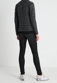 Sort pufferjakke med vandret quiltning, slim-fit sorte jeans og sølvfarvede sportssko. Jakken har høj krave og albuelapper.