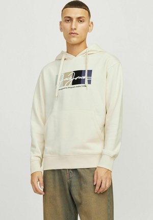 Sudadera color crema con bolsillo frontal, capucha ajustable con cordón y logotipo gráfico en azul oscuro y beis en el pecho.