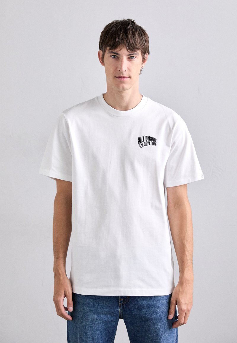 Tricou alb din bumbac, cu guler rotund și mâneci scurte, cu un logo negru imprimat pe pieptul stâng. Purtați cu blugi albaștri.