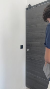 Sötét fa textúrájú tolóajtó vízszintes vonalakkal, kör alakú fogantyúval. Fekete faliswitch a mellette lévő fehér falon.