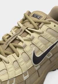 Baskets beige Nike avec des panneaux en mesh et en cuir, logo Swoosh noir, et lacets comportant le texte "BONTERMAN SERIES" sur une bride.