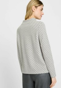 Langarmshirt aus leichtem Stoff mit einem geometrischen Muster von schwarzen Kreisen auf weißem Hintergrund, mit lockerem Schnitt und runder Ausschnitt.