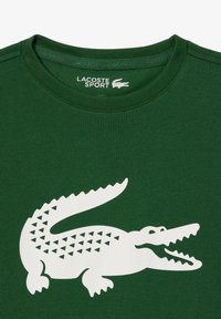 T-shirt en coton vert avec un grand logo de crocodile blanc présentant un motif triangulaire. Design à col rond avec des détails cousus.