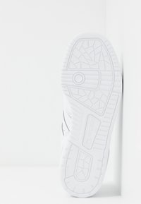 Scarpa sportiva bianca con suola in gomma texturizzata, caratterizzata da un motivo geometrico e dettagli neri sui lati.