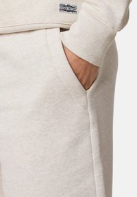 Ljusbeige sweatshirt med en mjuk textur, som har en ribbad manschett och en synlig sidoficka. Inkluderar en märkesetikett på bröstet.