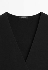 Indumento in tessuto nero texturizzato con scollo a V profondo, caratterizzato da un'etichetta "Massimo Dutti Made in China" all'interno del colletto.