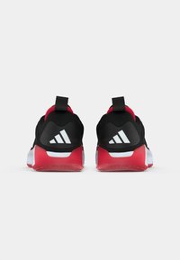 O pereche de pantofi sport negri și roșii cu tălpi albe și logo-ul Adidas pe călcâi, văzuți din spate pe un fundal alb.