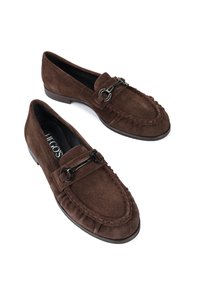 Brązowe zamszowe loafersy mają wszyty design mokasynów, dekoracyjny metalowy łańcuszek oraz płaską, trwałą gumową podeszwę.