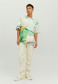 Camicia a maniche corte con bottoni, stampata con foglie e paesaggi multicolori, abbinata a pantaloni tapered color crema e sneakers beige.