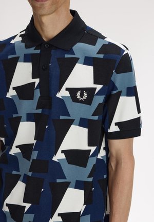 Man draagt een poloshirt met korte mouwen, zwarte kraag en geometrisch patroon in blauw, zwart en wit, met een klein wit laurierkranslogo.