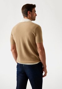 Polo cu mânecă scurtă dintr-un material tricotat bej, cu un guler alb în contrast; asortat cu blugi negri din denim, având un finisaj texturat.