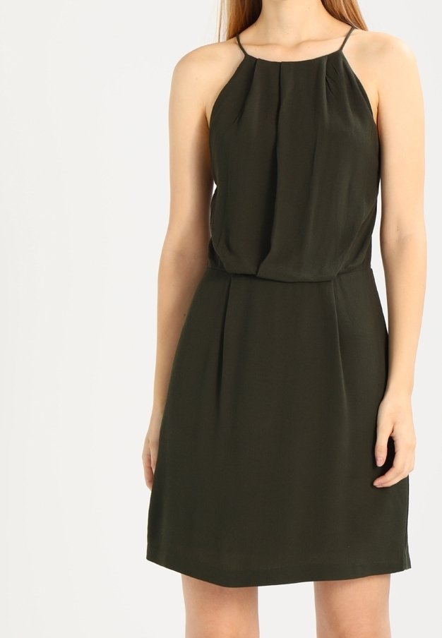 Femme portant une robe sans manches, de couleur vert foncé, arrivant au genou, avec des bretelles fines et un corsage ample et plissé.
