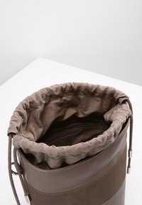 Borsa a secchiello in pelle marrone con fodera in tessuto morbido, chiusura a cordoncino e forma circolare. Presenta una texture liscia e un design minimalista.
