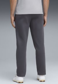 Šedé tepláky s rovnym strihom, vyrobené z mäkkej tkaniny. Majú elastický pás a jednoduché šitie, v kombinácii s bielymi športovými topánkami.