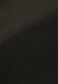 Gros plan sur un tissu noir avec un motif de sergé diagonal fin, montrant une texture subtile et des variations de lumière et d’ombre.
