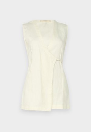 Haut sans manches en lin crème clair, présentant un décolleté en V, un détail découpé incurvé sur le côté et une coupe décontractée aux lignes épurées.