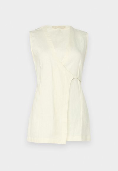 Top sem mangas em linho creme claro, com decote em V, detalhe recortado curvo de lado e um corte solto com linhas limpas.