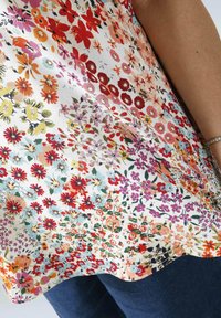 Floral blouse featuring a white background with multicolored flowers in red, pink, yellow, and blue. Smooth fabric, curved hemline.