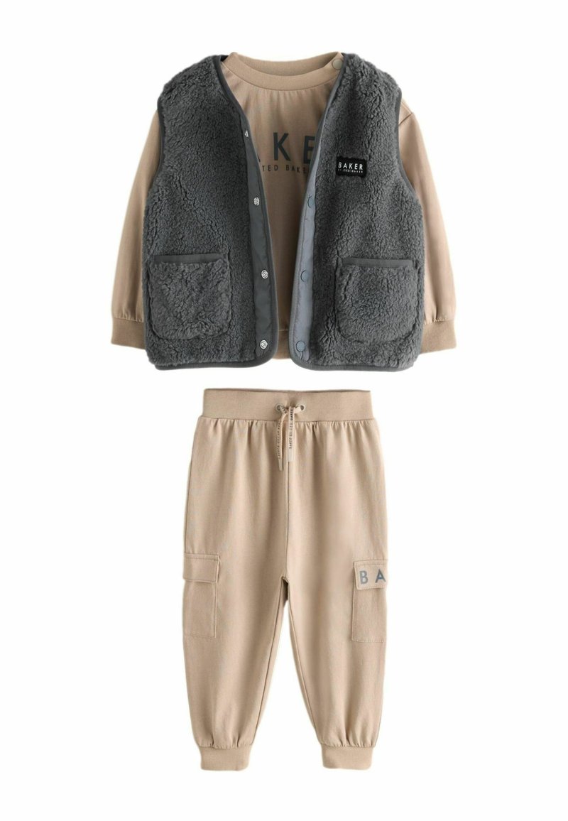 Dvoudílný outfit složený z šedé, huňaté vesty se cvoky a dvěma kapsami, spárovaný s béžovými jogger kalhotami s elastickým pasem a postranními kapsami.