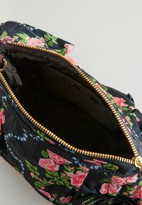 Svart blomsterhandväska med rosa rosor, en strukturerad textil, gyllene dragkedja och innerficka, som visar en rymlig, fodrad avdelning.