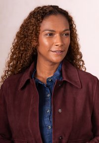 Burgundy suede jacket with a collared neckline, front snap closure, and two side pockets layered over a blue button-down shirt.