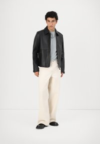 Sort læderjakke med lynlås, parret med en lyseblå t-shirt og off-white bukser med bred ben. Sorte sko fuldender looket.