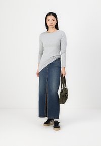 Sivý top s dlhým rukávom skombinovaný s modrou denimmovou maxi sukňou s predným rozparkom, doplnený o čierne tenisky a olivovo zelenú tašku.