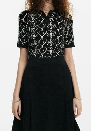 Black polo shirt featuring a textured design of white hearts and bows. Short sleeves and a three-button placket complete the style.