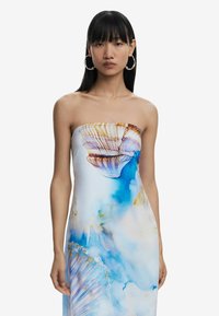 Õlgtuidev kleit pehmest kangast, millel on sinine ja valge abstraktne muster ja kestamotiivid. Mudel kannab põimnõelu, mis viitab elegantsusele.