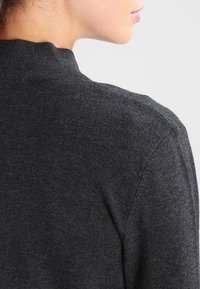 Mörkgrå, texturerad tröja med hög krage, som visar en minimalistisk design och mjukt tyg, sedd bakifrån.