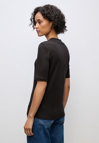 Sort bomulds T-shirt med korte ærmer, rund halsudskæring og en afslappet pasform. Båret med blå denim jeans, der har en simpel, glat tekstur.